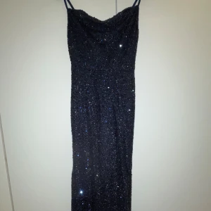 Svart glittrig långklänning - Säljer en svart långklänning med tunna axelband och glittrigt material som verkligen fångar ljuset. Klänningen har en smickrande rak siluett och är perfekt för dig som vill sticka ut med en elegant och glamorös look. Passar dig som gillar att glänsa på dansgolvet.