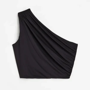 Svart oneshoulder topp - Säljer en svart oneshoulder topp med snygg drapering och elastisk kant upptill. Toppen är croppad och har en cool asymmetrisk design som ger en trendig vibe. Perfekt att styla med höga jeans eller kjol för en stilren look.