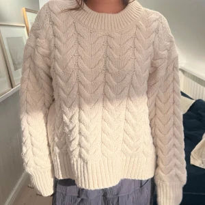 Vit stickad kabeltröja oversize  - Säljer en vit stickad tröja med grovt kabelmönster och rund hals. Tröjan har långärmade ärmar och breda ribbade muddar vid hals, ärmslut och nederkant. Perfekt för dig som gillar mysiga och chunky tröjor med lite oversized känsla.