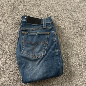 Blå jeans Tiger of Sweden 26/32 - Snygga blå jeans från Tiger of Sweden i klassisk femficksmodell. Jeansen har orangea kontrastsömmar, knapp och dragkedja fram samt bälteshällor. Passar dig som gillar stilrena och tidlösa jeans med en modern touch.