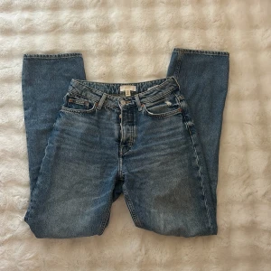 Blå ripped jeans från H&M, strl 36 - Säljer ett par blå jeans från H&M i storlek 36 med raka ben och höga midja. Jeansen har snygga slitningar och stora hål med fransar på båda benen för en cool, avslappnad vibe. Klassisk femficksmodell med knapp och dragkedja framtill.