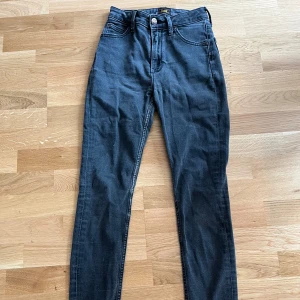 Gråsvarta skinny jeans från Lee Ivy W26 L31 - Snygga gråsvarta jeans från Lee, modell Ivy, med skinny passform och hög midja. Klassisk femficksdesign, silverfärgad knapp med Lee-logga och dragkedja. Välanvända men har fortfarande lite kvar att ge. Köpte dem begagnade men tyvärr är de för små för mig. 