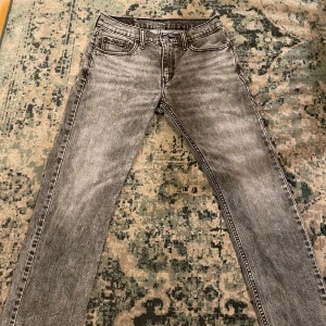 Levi's 502 grå jeans straight fit 30,30 - Säljer ett par gråa Levi's 502 jeans med klassisk straight fit och fem fickor. Jeansen har en cool tvättad look, knappgylf och den ikoniska läderpatchen bak i midjan. Passar dig som gillar tidlös stil och vill ha ett par jeans som funkar till allt.