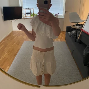 Krämvit kjol från Zara - Säljer en krämvit kjol från Zara. Banden på kjolen har fina stenar på sig. Materialet är mjukt och lätt, perfekt för varma dagar. Snygg och feminin stil som ger en fräsch vibe.