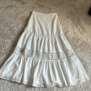 Vit långkjol med spets från Cider - Superfin vit långkjol från Cider i storlek XXS. Kjolen har flera lager med volanger och detaljerad spets som ger en romantisk vibe. Säljer pga att jag aldrig använder den, och den bara är i garderoben.