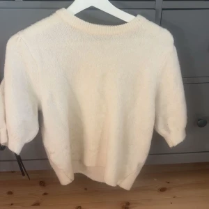 Vit stickad tröja med kort ärm - Mysig vit stickad tröja med rund hals och korta ärmar. Perfekt för lager-på-lager och passar till både jeans och kjol. Tröjan har en enkel och clean look med ribbad kant vid halsen och nederdelen.