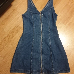 Jeansklänning med dragkedja - Snygg jeansklänning i blå denim med markerade sömmar och en cool dragkedja framtill. Klänningen är ärmlös och har en v-ringad hals. Använd 1 gång. Storlek 36💙