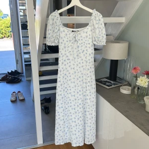 Vit blommig långklänning från Gina Tricot - Supersöt långklänning från Gina Tricot i vitt med ljusblått blommigt mönster. Klänningen har puffärmar, smockad överdel och knyt framtill. Perfekt för sommarens alla tillfällen! Materialet är mjukt och bekvämt, och modellen är feminin med en rak hals 🤍🤍oanvänd 