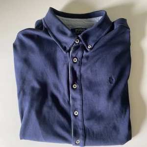 Mörkblå skjorta från Polo Ralph Lauren - Snygg mörkblå skjorta från Polo Ralph Lauren i mjuk bomull (100%) och långa ärmar. Skjortan är storlek L, 14-16 i barnstorlek, vilket motsvarar storlek S/XS i vuxenstorlek. | Skick: 9 / 10, väldigt sparsamt använd | Nypris: ~1200 | Vårt pris: 499 | Storlek: S/XS | Tveka inte att höra av er för fler bilder eller funderingar!