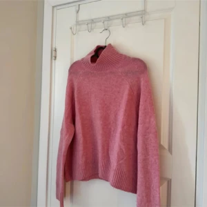 Rosa stickad polotröja med ribbad krage - Mysig rosa polotröja med bred ribbad krage och långa ärmar. Tröjan är stickad och har en loose passform med ribbade muddar vid ärmslut och nederkant . Perfekt att matcha med jeans för en chill look. Lite nopprig 