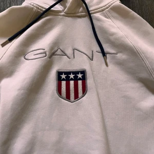 Vit hoodie från GANT med emblem - Säljer en vit hoodie från gant vet ej storlek riktigt men jag har small på dom flesta kläder eller medium men denna är lite för liten så skulle gissa small fast tvätten gjort lite mindre eller tajtare då