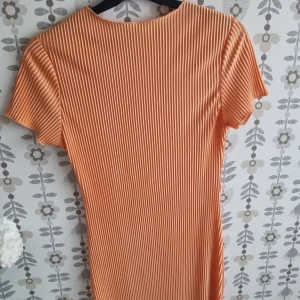 Ribbad orange kortklänning - Säljer en snygg ribbad kortärmad klänning i en fräsch orange färg. Klänningen har en tight passform och är tillverkad i ett mjukt, ribbat material som ger en cool struktur. Perfekt för dig som gillar färg och vill sticka ut lite extra.