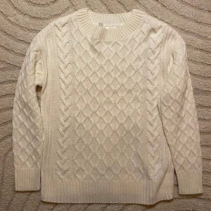 Vit stickad tröja från bpc - Säljer en vit stickad tröja från bpc med snyggt flätmönster och diamantstruktur på både fram- och baksida. Tröjan har rund hals, ribbade muddar och långärmade. Perfekt för dig som gillar klassisk och clean stil.