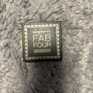 Makeup Mekka Fab Four ögonskuggspalett - Snygg ögonskuggspalett från Makeup Mekka med fyra nyanser: matt beige, skimrande guld, varm ljusbrun och djup mörkbrun. Kommer i en svart fyrkantig dosa med spegel i locket, perfekt för att skapa både naturliga och intensiva looks.