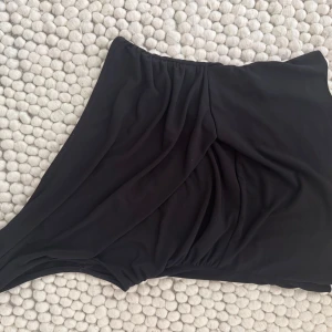 Svart asymmetrisk topp - Snygg svart topp med asymmetrisk design och draperade detaljer framtill. Perfekt för dig som vill ha en stilren och modern look. Materialet är mjukt och följsamt för bästa komfort.
