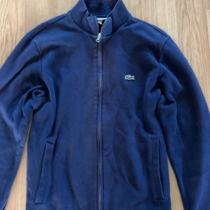 Marinblå ziphoodie från Lacoste - Snygg marinblå ziphoodie från Lacoste som inte har några defekter! Normal i storlek 