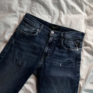 Replay mörkblå jeans straight fit - Snygga mörkblå jeans från Replay med klassisk femficksdesign och diskreta slitningar. Modellen har raka ben och normal passform, perfekt för dig som gillar en clean och tidlös look. Jeansen är gjorda i slitstarkt denim och har Replay-logga på fickan.
