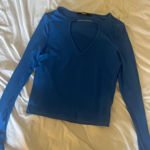 Blå långärmad topp med strassdetalj - Snygg blå långärmad topp från Bik Bok i stretchigt material. V-ringad hals med strassdetalj som ger en extra touch. Perfekt att styla med jeans eller kjol för en cool look. Passformen är normal och tyget känns mjukt mot huden.