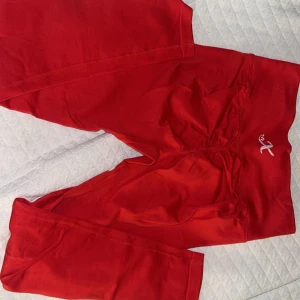 Röda träningsbyxor med scrunch från X - Säljer ett par röda träningsbyxor från X med scrunch-detalj bak och liten broderad logga på höften. De är tighta och har hög midja, perfekta för gymmet. Materialet är mjukt och stretchigt för maximal komfort. Formar bra! 😇