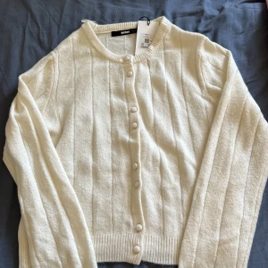Vit stickad kofta från Bikbok - (Prislapp fortfarande på) Säljer en vit stickad kofta från Bikbok i storlek S. Koftan har rund hals, ribbade muddar och knappar framtill i samma färg som plagget. Materialet är mjukt och har en diskret ribbad struktur. Perfekt för lager-på-lager och chill stil.