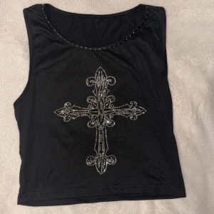 Svart croppad linnetopp med strasskors - Snygg svart croppad linnetopp med ett stort kors i strass framtill. Säljer då jag ej använder den längre ✨ Köpt från AliExpress, sitter som S