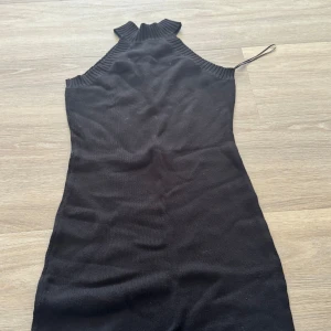Svart stickad ärmlös klänning - Säljer en svart stickad klänning med hög hals och ärmlös design. Klänningen har en tight passform och är perfekt för dig som gillar en stilren look. Enkel att styla med smycken eller en snygg jacka.