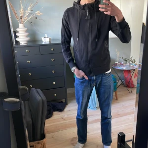 Svart sweet shirt - Säljer en svart sweatshirt med ikoniska goggles i luvan. Den har justerbar huva med snörning. Perfekt att ha som supporter eller bara vill ha lite stil i vardagen