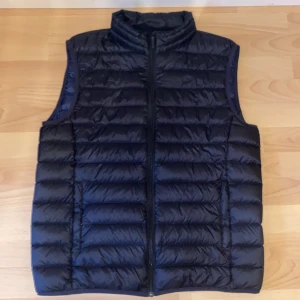 Svart dunväst från Dressmann - Säljer en svart dunväst från Dressmann med hög krage och dragkedja framtill. Västen har en quiltad design och är perfekt för lager-på-lager-stil under kyliga dagar.