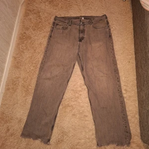 Grå Weekday jeans Loose Straight - Säljer ett par väldigt slitna grå jeans från Weekday, modell Glaky Loose Straight. Båda främfre fickorna har hål i sig. Byxorna har raka ben, fem fickor och råa kanter nertill. Klassisk dragkedja och knappstängning framtill. Perfekta för en avslappnad stil.