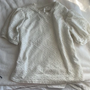 Vit spetsblus från Object - Säljer en vit blus från Object med vackert spetsmönster och puffiga korta ärmar. Blusen har en feminin och romantisk känsla med fina detaljer i tyget. Perfekt att styla till olika tillfällen!