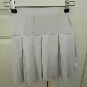 Vit/blå kortkjol - Säljer en vit/blå kortkjol med medel midja. Kjolen har klassiska veck och en enkel, stilren design som passar perfekt till sneakers eller boots. Superenkel att matcha med olika toppar för en trendig look. Pris går att diskutera och ställ en fråga om ni har en!!!