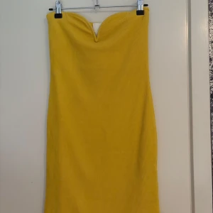 Gul ribbad axelbandslös klänning - Säljer en axelbandslös gul klänning med ribbad struktur och hjärtformad urringning. Klänningen är figurnära och har en enkel, stilren design som passar perfekt till sommaren.