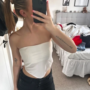 Vit tubtopp från BikBok - Säljer en vit tubtopp från BikBok i storlek S. Toppen är axelbandslös och har en snygg, spetsig nederkant framtill. Materialet är mjukt och stretchigt. Fint skick!