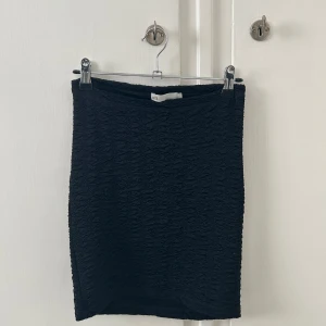 Svart tight kjol - Svart tight kjol från Åhléns med strukturerat tyg. Kjolen är kort och har en enkel, stilren design som passar perfekt till många olika outfits. Använd en gång, i nyskick!