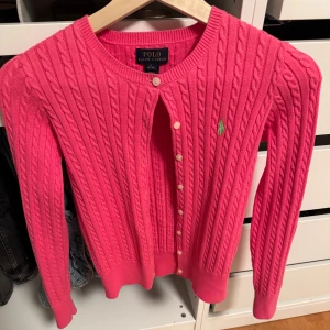 Rosa kabelstickad kofta från Polo Ralph Lauren - Säljer en rosa kabelstickad kofta från Polo Ralph Lauren med grön broderat logotyp på bröstet💗är i väldigt bra skick och inte andvänd så många gånger❤️