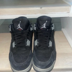 Svarta Nike Air Jordans 4 Retro - Säljer ett par svarta Nike Air Jordans 4 Retro med grå och vita detaljer. Skorna har klassisk snörning, rund tå och platt sula. Ikonisk Jumpman-logga syns både på plösen och hälen. Perfekta för dig som gillar streetwear och sneakers med attityd. Använda få gånger håller ett bra skick.