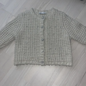 Beige stickad kofta  från Zara - Superfin beige stickad kofta från Zara med pärlknappar och små pärldetaljer över hela tröjan. Koftan har lång ärm och ett mysigt, chunky material som känns lyxigt. Perfekt att styla till jeans eller kjol.
