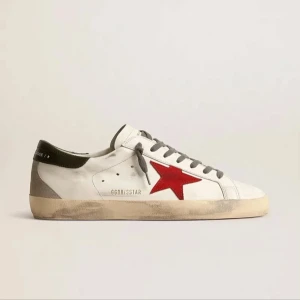 Golden goose - Säljer ett par vita sneakers från Golden Goose med en röd stjärna på sidan och grå detaljer vid hälen. Skorna har grå snörning och en platt sula. Perfekta för dig som gillar en sportig och trendig stil. Priset kan diskuteras. Skriv för minsta lilla frågan💪🏽