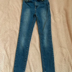 Blå skinny jeans - Säljer ett par klassiska blå skinny jeans med normal passform och hög midja. Jeansen har fem fickor, dragkedja och knapp framtill. Perfekta till vardags och lätta att matcha med olika toppar.