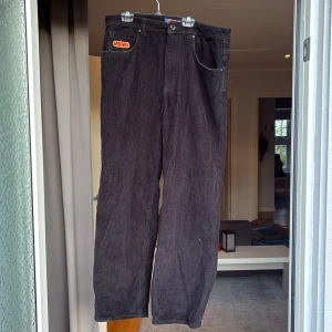 Svarta manchesterbyxor från Empyre - Svarta manchesterbyxor från Empyre med raka ben och klassisk femficksdesign. Byxorna har ett färgglatt broderat märke på fickan och midjebandet. Tillverkade i mjuk manchester med baggy passform. Det är ett hål i byxan därav priset