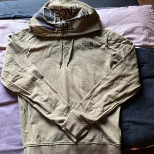 Beige hoodie från The North Face - Säljer en beige hoodie från The North Face med stor logga på huvan och mindre logga på bröstet. Tröjan har långa ärmar, ribbade muddar och klassisk huva. Perfekt för en avslappnad stil.