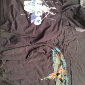 1300kr för båda 1500kr styck - Säljer en svart hoodie från Hugo med stort tryck av en insekt och texten 'HUGO' i vitt och blått på framsidan. Tröjan har huva med dragsko och en klassisk passform. Perfekt för dig som gillar unika tryck och streetwear. Och en marcelo hoddie 