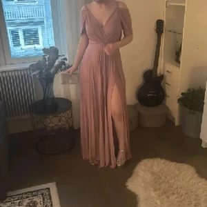 Perfekta balklänningen❤️ - Säljer en elegant långklänning i dusty rosa med v-ringning, öppen rygg och slits framtill. Klänningen har offshoulder-ärmar och ett fint fall. Perfekt för bal eller fest! Materialet känns mjukt och följsamt. Så snygg och formar kroppen så så fint😁 från Asos som är helt slutsåld❤️ Lappar kvar på den så helt ny. Strl s men passar även M då den är stretchig. Jag på bild är 1.58 med klack ca 10 cm😁