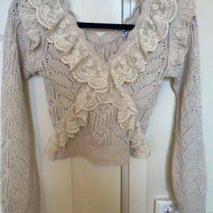 Beige stickad tröja med spetsvolang från Zara - Luftig långärmad topp från Zara i storlek S. Fin och bekväm modell med volangdetaljer som korsar över framsidan. Perfekt för en stilren vardagslook eller för festligare tillfällen. Använd sparsamt och i mycket fint skick utan fläckar eller skador. Modellen finns inte längre att köpa i butik. Hör av dig om du har några frågor!