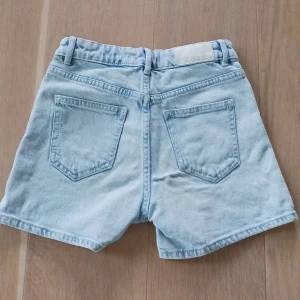 Ljusblå jeansshorts från Lindex -  Shortsen har knapp och dragkedja framtill samt raka ben. Perfekta för varma dagar och enkel att matcha med olika toppar. De är i storlek 10-11 år! Skriv bara vid frågor och fler bilder!❤️