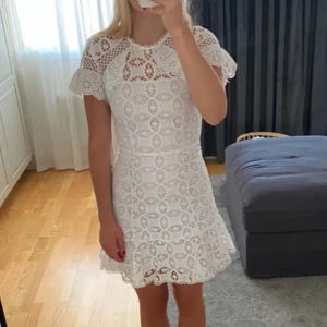 Sandro Studentklänning  - Superfin vit kortklänning i spets med volangdetaljer och korta ärmar. Klänningen har ett vackert hålmönster och rund halsringning. Perfekt för studenten eller andra tillfällen! Inget tecken på användning förutom en lite fläck (bild 3) Pris kan diskuteras! 💗