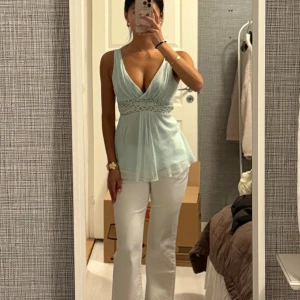 Ljusblå ärmlös omlottopp - Säljer en ljusblå ärmlös omlottopp med djup v-ringning och markerad midja med dekorativt band. Man knyter banden i bak på ryggen. Skitsnygg sommar färg! 