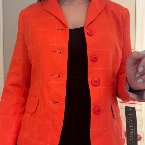 Orange rutig kavaj från Pendleton - Säljer en orange/rosa kavaj från Pendleton med rutigt mönster och knappar framtill. Kavajen har en liten hål i tyget (se bild). Köpte på rea i USA men kom aldrig till användning. Ordinarie pris var $280 men jag köpte den för $20. Storlek 4 (motsvarande S) och säljer för 50kr.