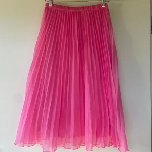 Plisserad rosa kjol från Divided - Säljer en plisserad långkjol i stark rosa färg från Divided. Kjolen har resår i midjan och är tillverkad i ett lätt, flowy material som ger ett snyggt fall. Perfekt för dig som vill sticka ut med färg.