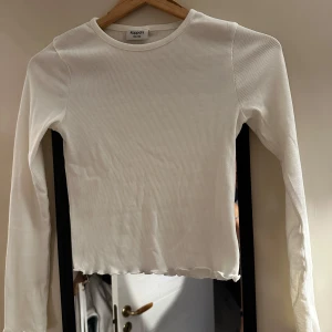 Vit ribbad långärmad tröja från Kappahl - Säljer en vit långärmad tröja från Kappahl i ribbat material. Tröjan har en enkel och stilren design med lätt vågig kant nertill. Perfekt till vardags och enkel att matcha med olika outfits.